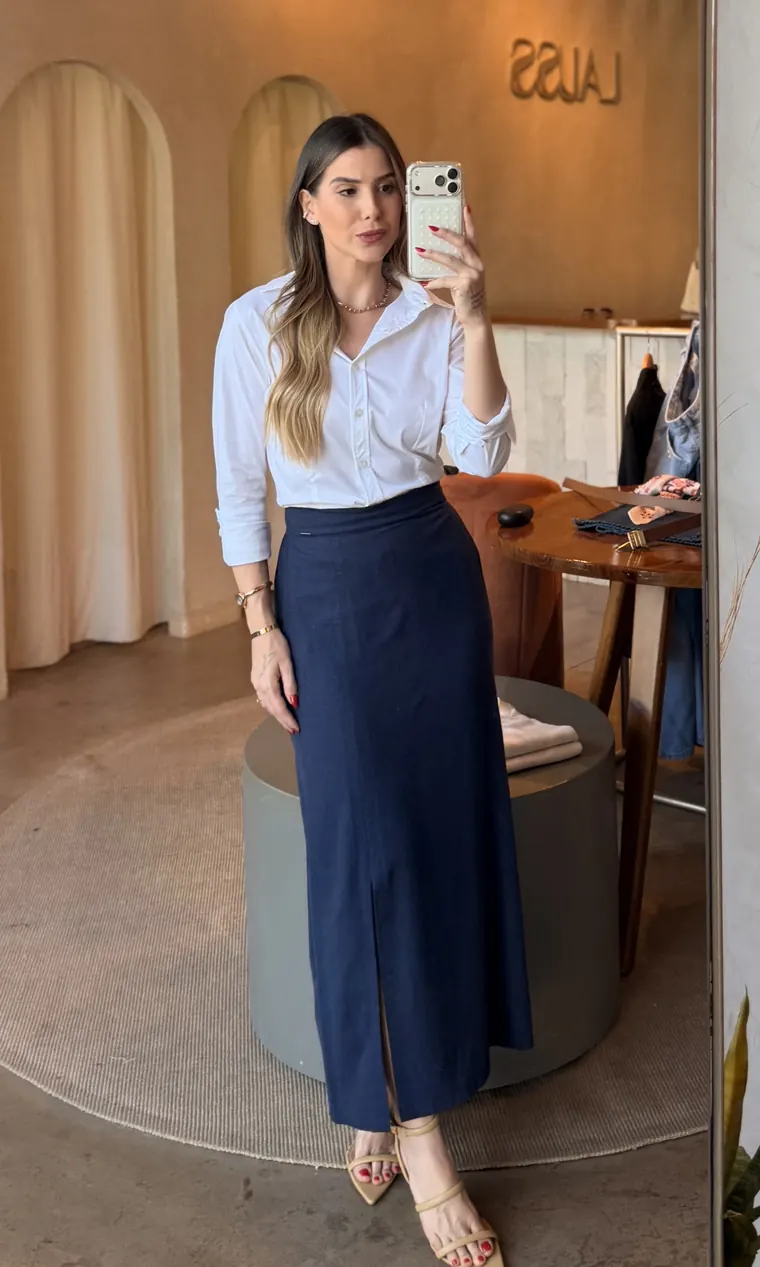 Ana de camisa branca e saia longa marinho com fenda, sandália de tiras nude